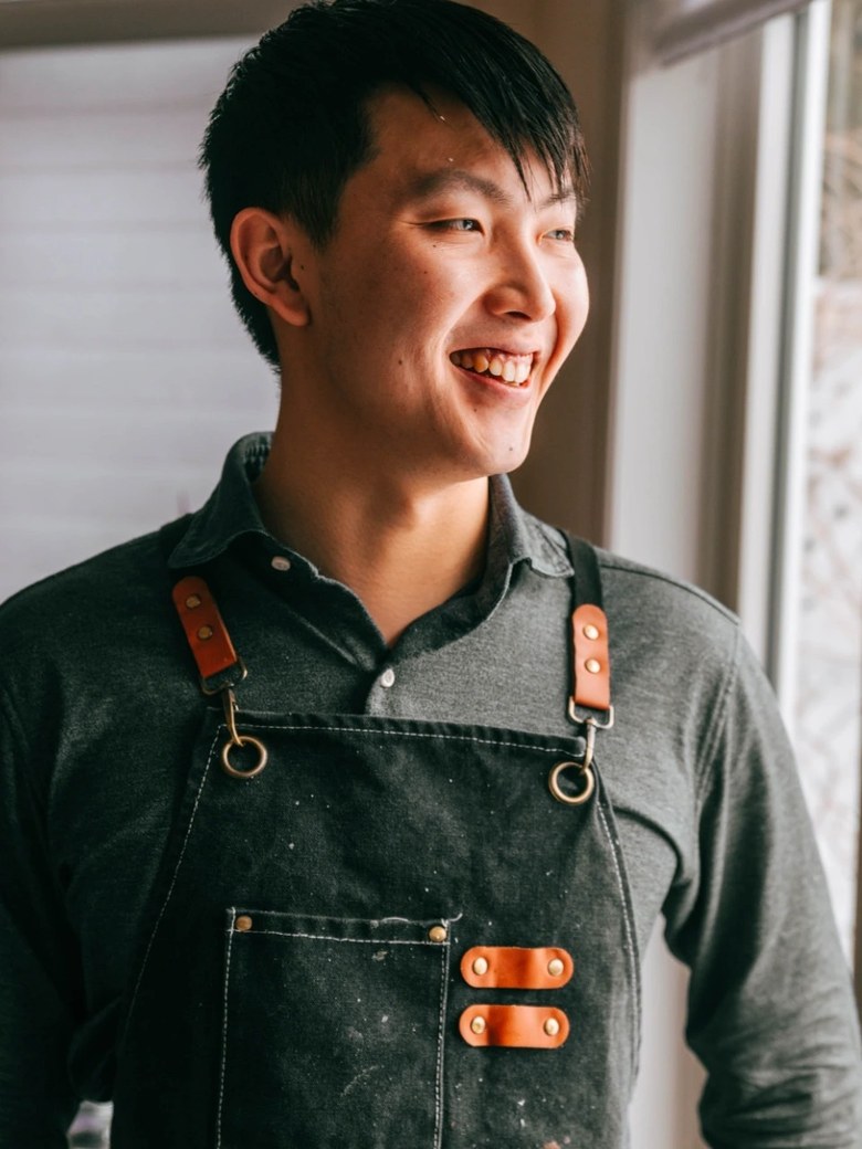 Sean Wang in a denim apron by a window, mid-laugh